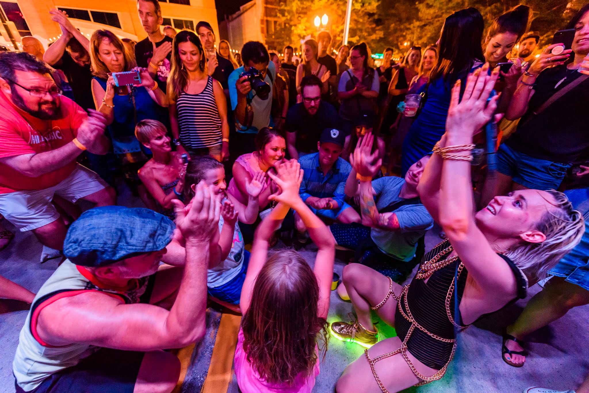 Crowd clapping and cheering at a nighttime outdoor event, with a woman in a black outfit dancing.