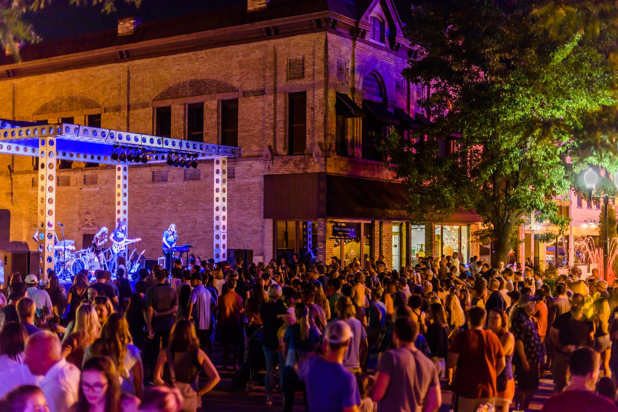 Outdoor concert at night with a band on stage and a large crowd gathered.