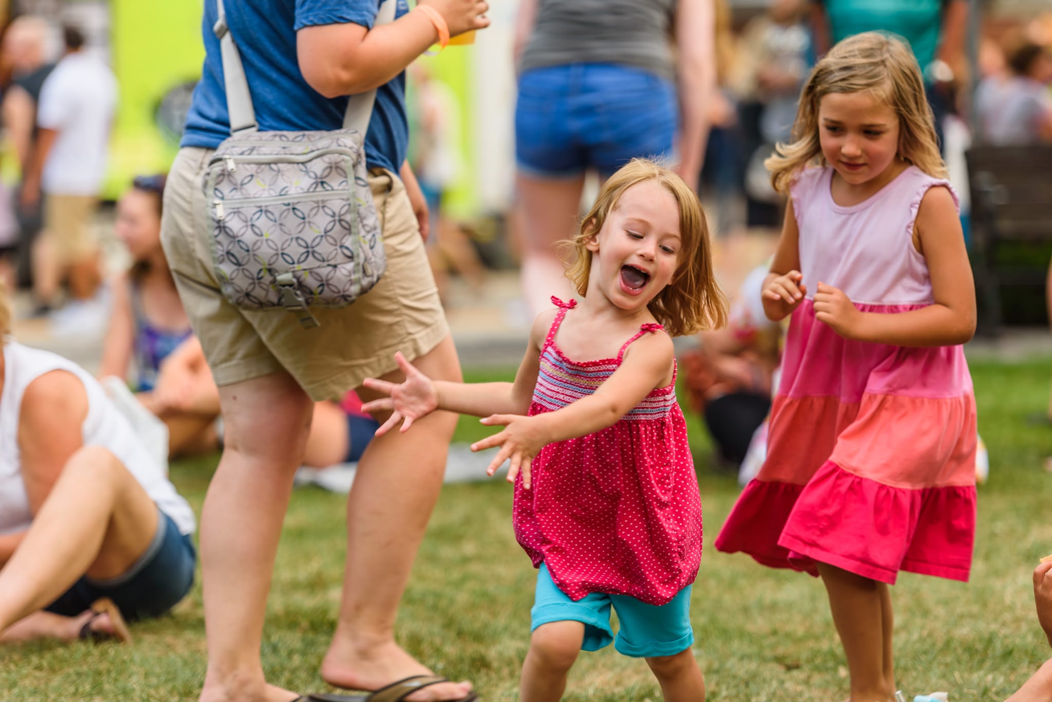 Two young girls dancing outdoors, one in a pink polka dot dress, the other in a tiered pink dress.