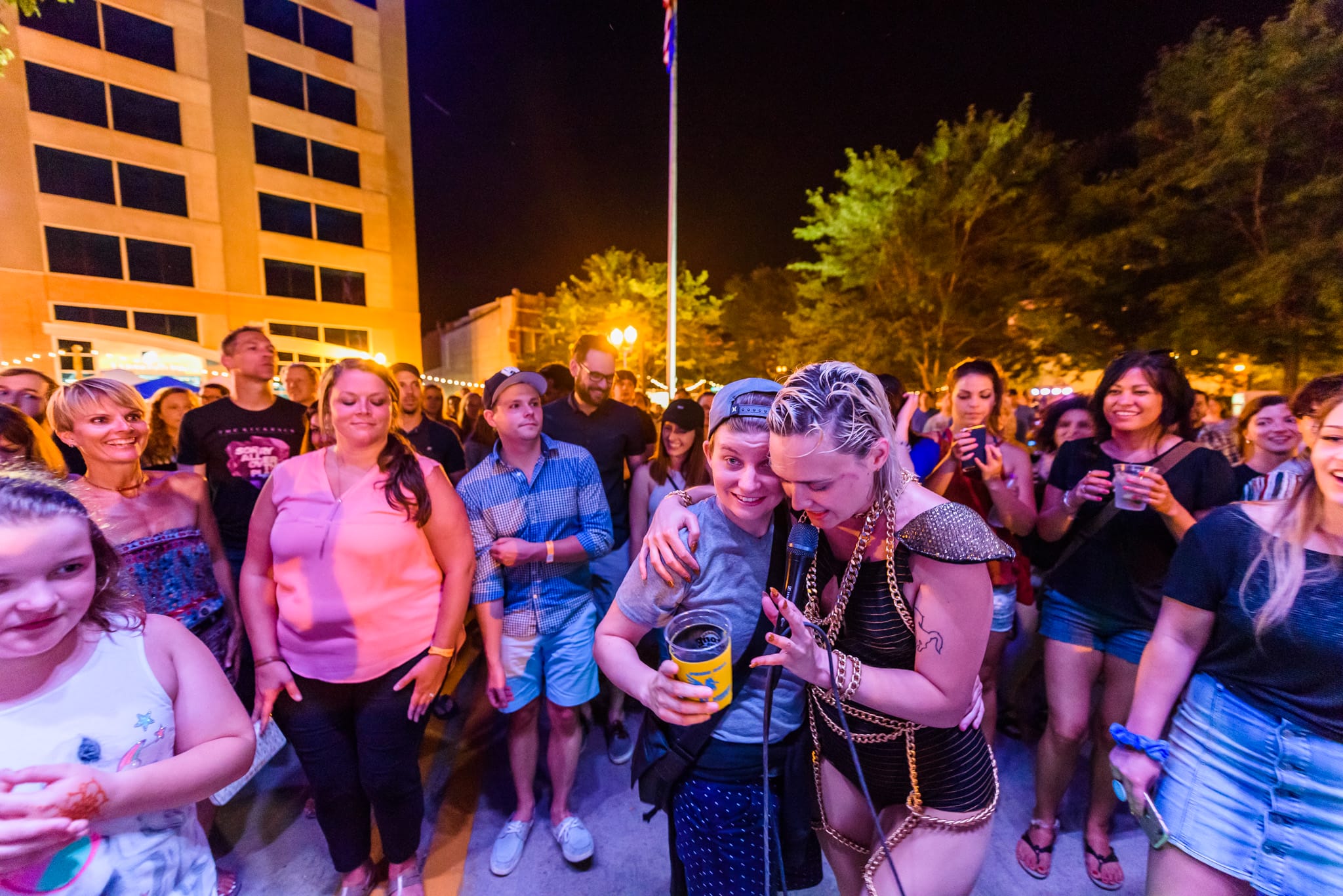 Two women embrace at a nighttime outdoor event, one holding a microphone.