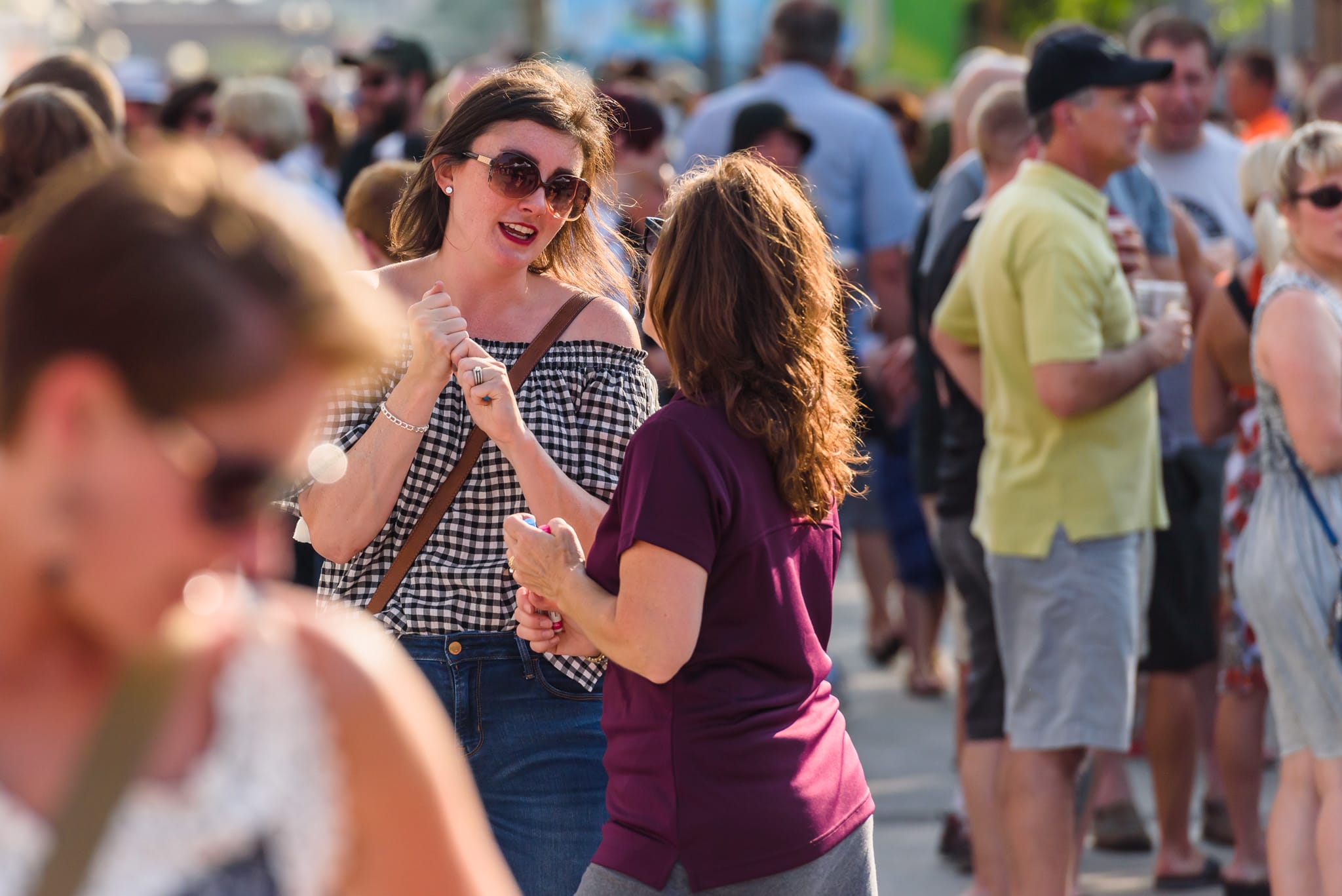 Two women in a crowd, one in a gingham top, talking and holding hands.