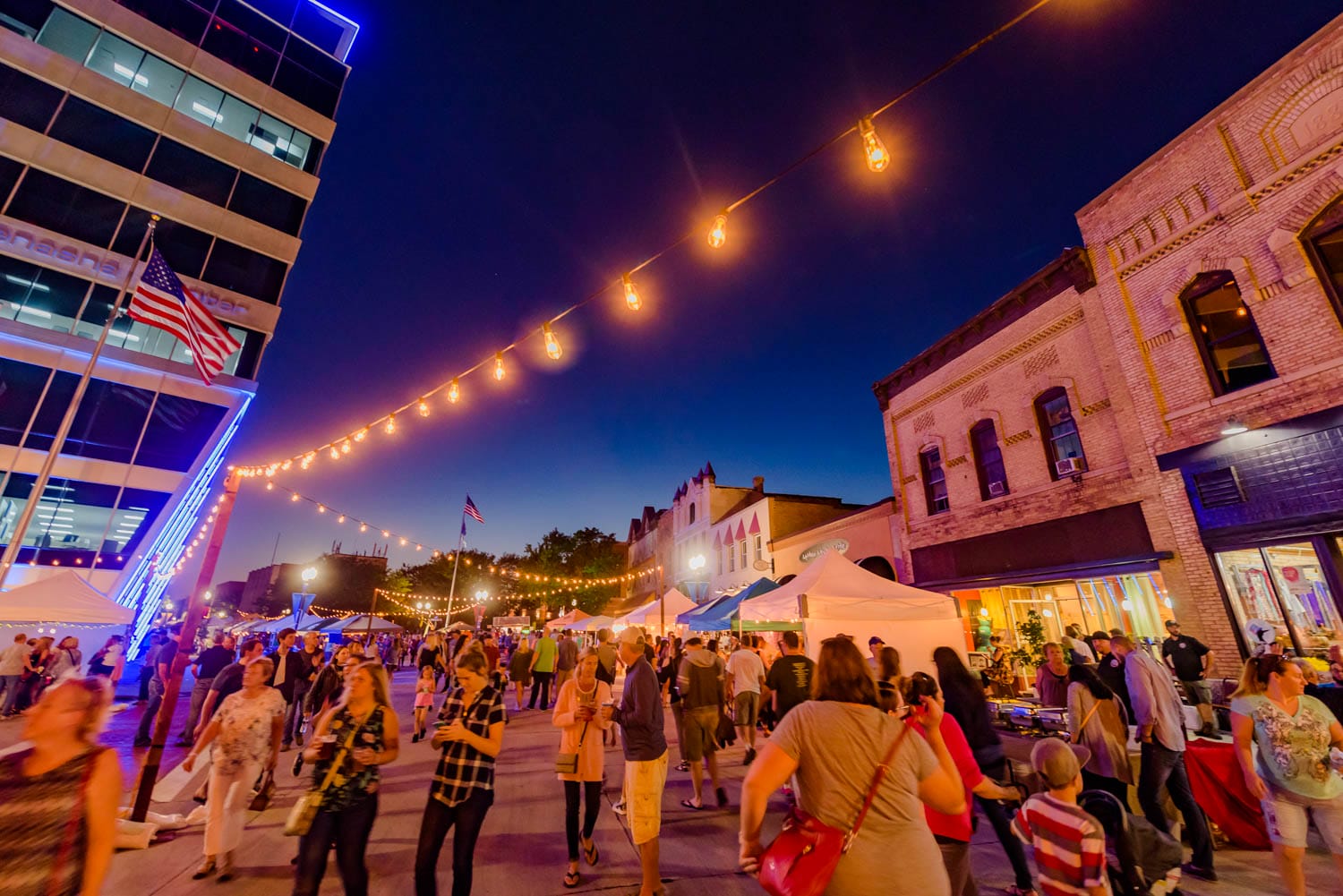 Street festival at dusk with string lights and crowds.