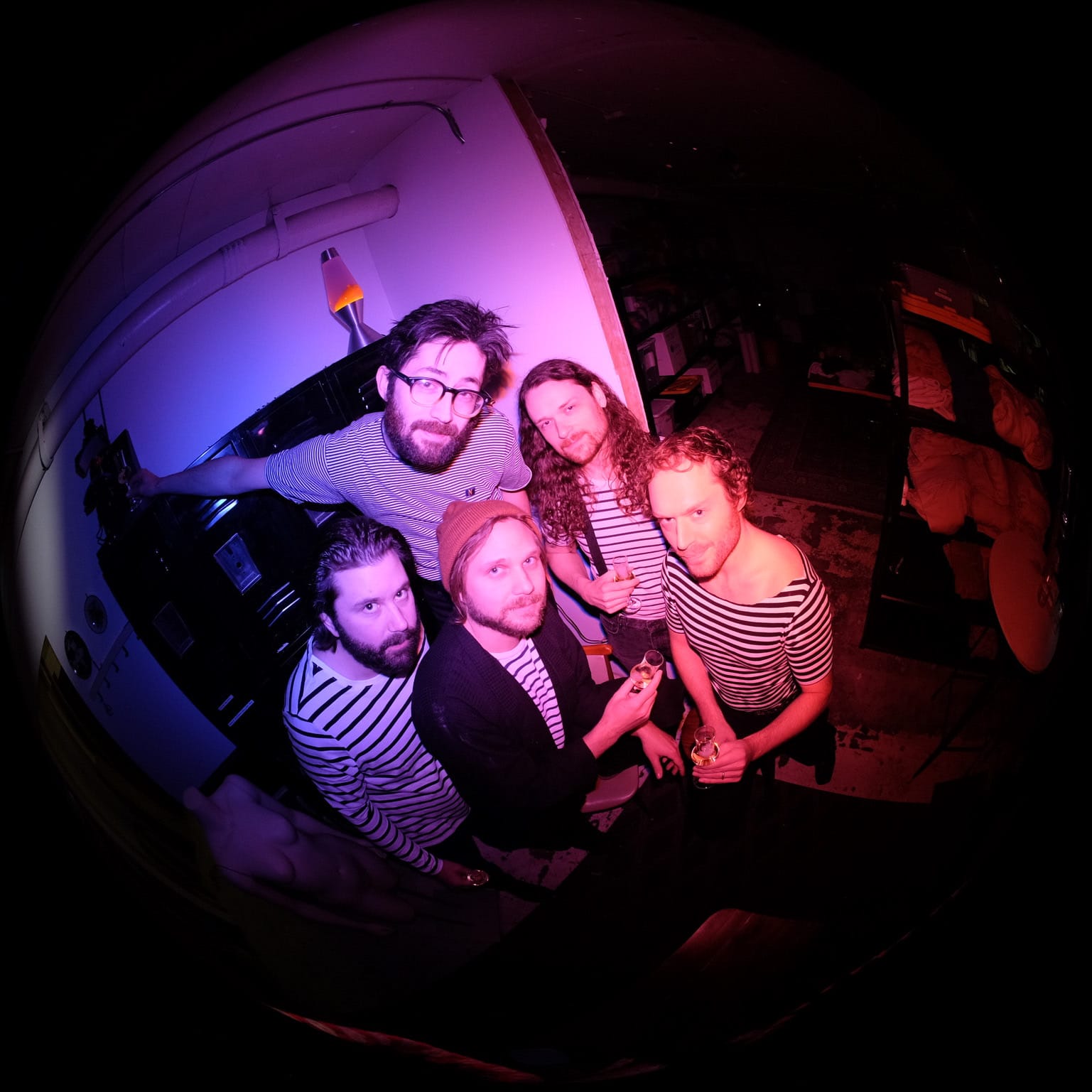 Five men in striped shirts pose for a fisheye lens photo, bathed in purple light.