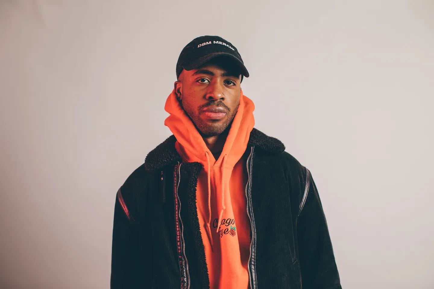 Man in black cap, orange hoodie, and black jacket.