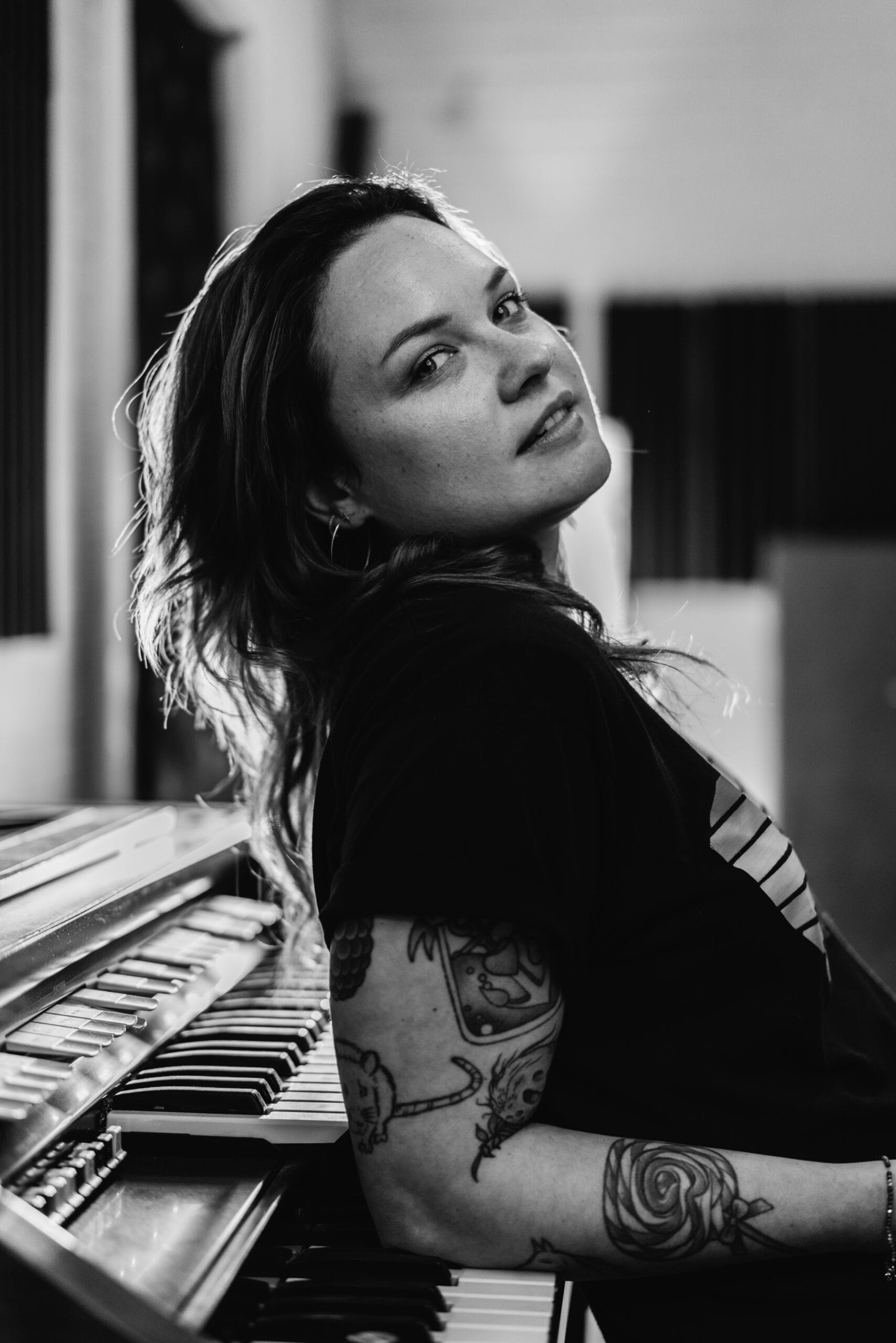 Woman with tattoos on her arm leans on a piano keyboard.