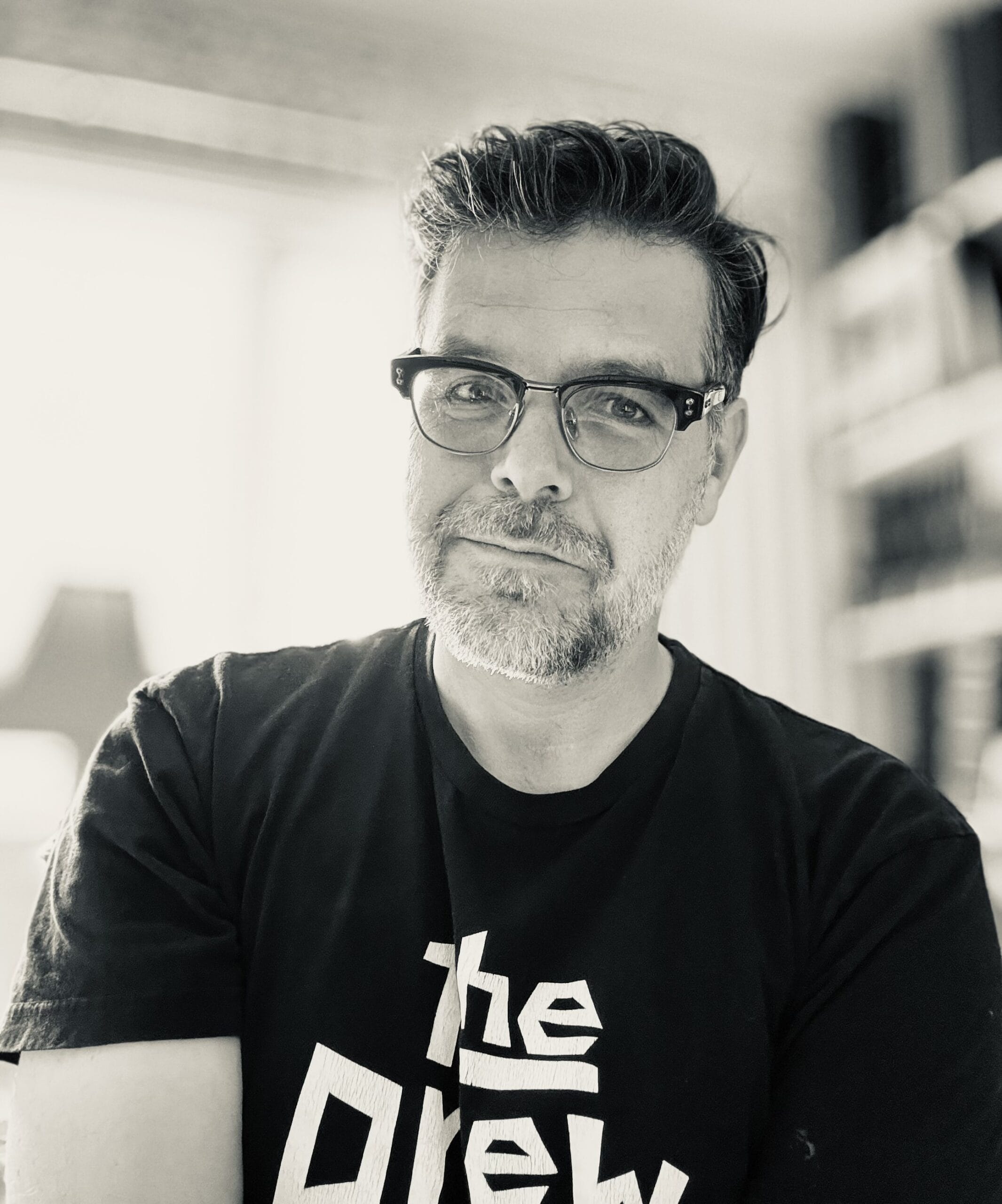 Man with glasses and beard wearing a black t-shirt with "the Drew" logo.